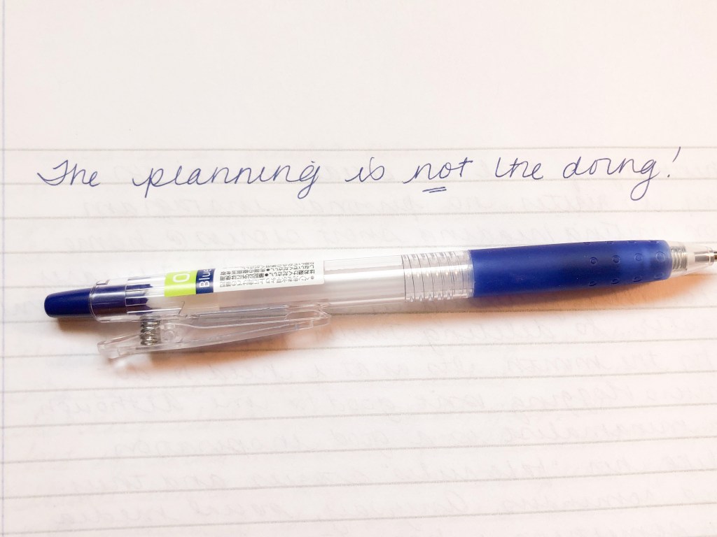 A notebook with a pen. The words above the pen say "The planning is not the doing."